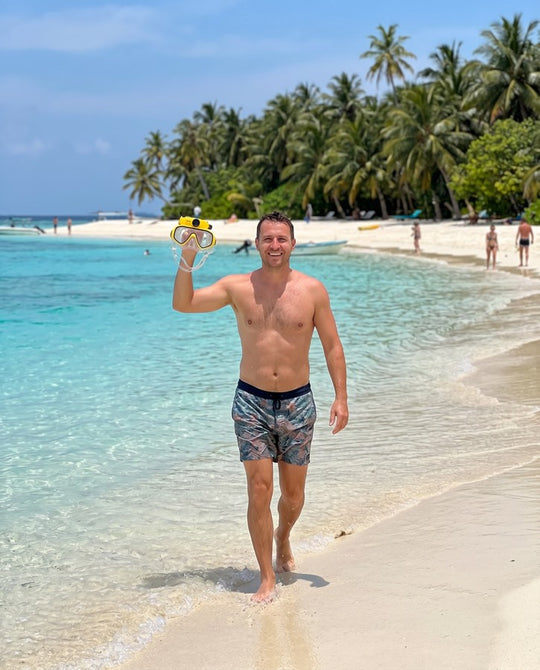 Man on a tropical beach holding up the yellow mask