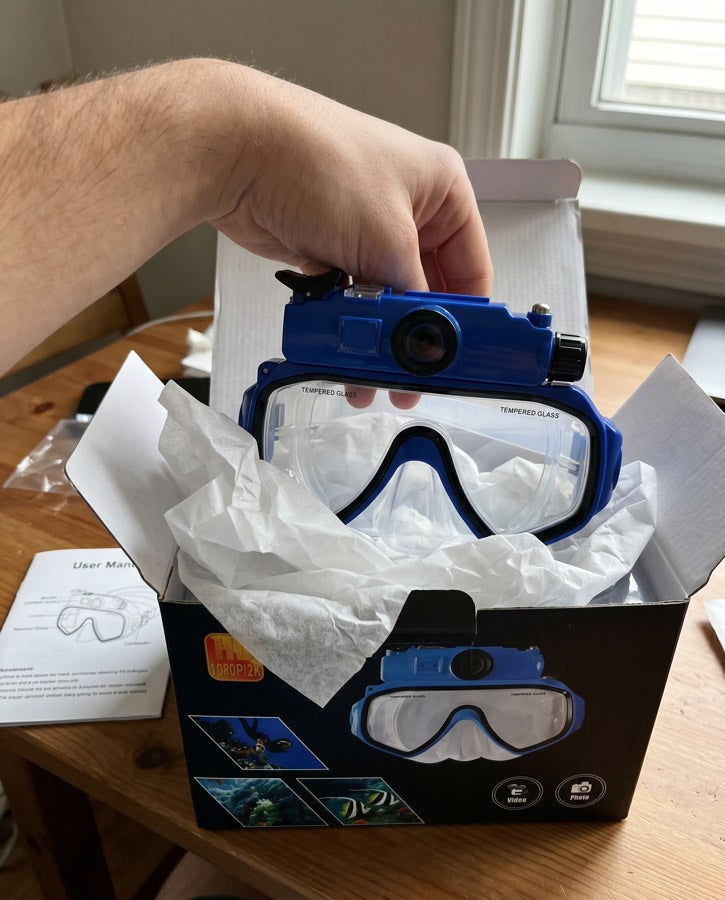 Hands lifting the blue Deep Dive Goggles out of its box