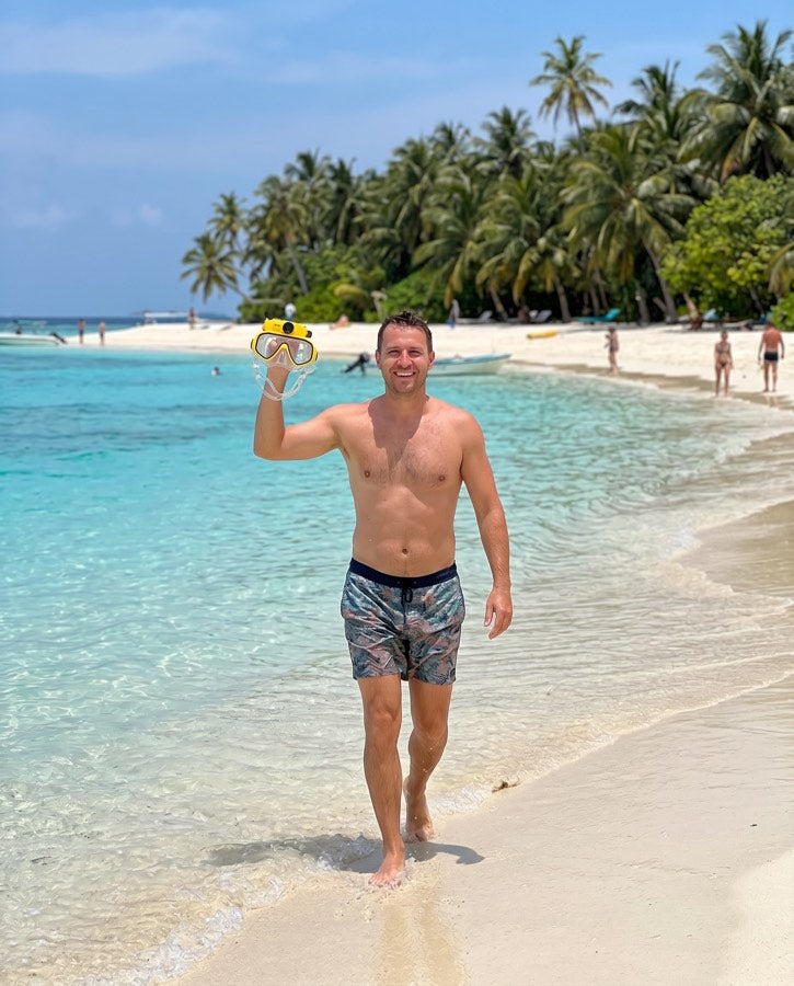 Man on a tropical beach holding up the yellow mask