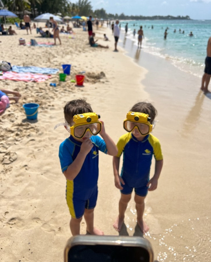 Two young boys in yellow masks and wetsuits on the beach