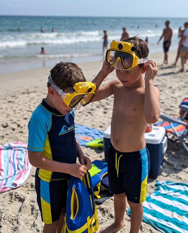 Boy helping another fit the yellow mask at the beach