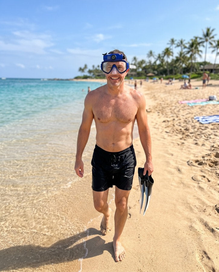 Man walking the beach in the blue mask, holding fins