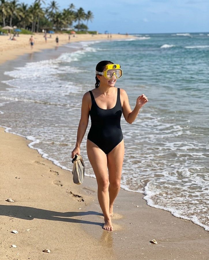 Woman walking off the beach holding fins, yellow mask on her head